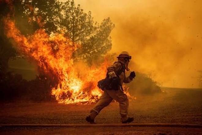 FILE - In this Tuesday, July 31, 2018, file photo, a firefighter runs while trying to save a home as a wildfire tears through Lakeport, Calif. The residence eventually burned. Authorities say a rapidly expanding Northern California wildfire burning over an area the size of Los Angeles has become the state’s largest blaze in recorded history. (AP Photo/Noah Berger, File)